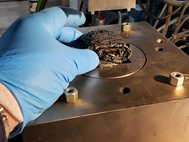 Image of technician's hand placing chopped glass fiber bundle into a compression molding tool, part of the frac lower slip production.